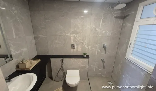 Modern bathroom interior at Purva Northern Lights 2 BHK featuring grey marble tiles, a wall-mounted toilet, and sleek black quartz ledge.