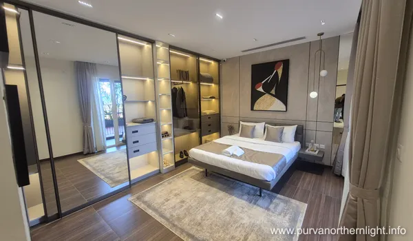 Modern bedroom interior at Purva Northern Lights showing a glass-door walk-in wardrobe with internal sensor lighting.