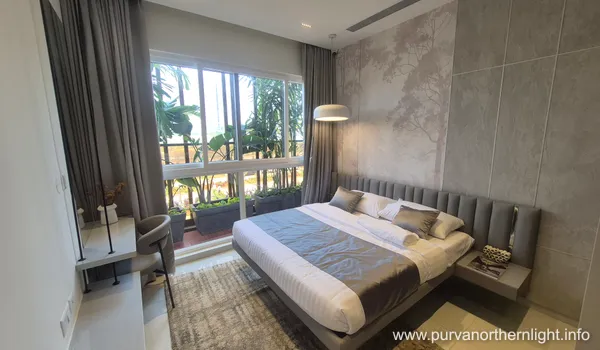 Elegant master bedroom at Purva Northern Lights with a grey fluted headboard and large windows overlooking a green balcony.