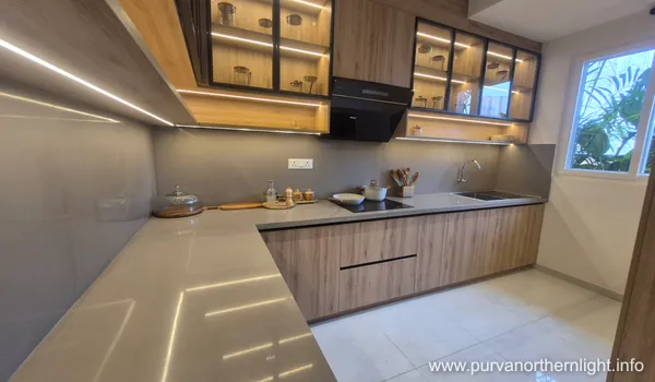 L-shaped modular kitchen at Purva Northern Lights with integrated LED cabinet lighting and wooden finish cabinetry.